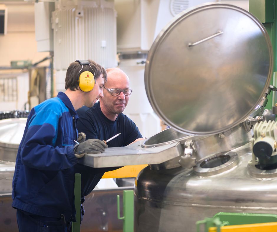 Vi är Westerlins, två kollegor står framför en kromfärgad maskin för grinding, dispersion, and mixing. En ikväll hörselkåpor och en iklädd skyddsglasögon.